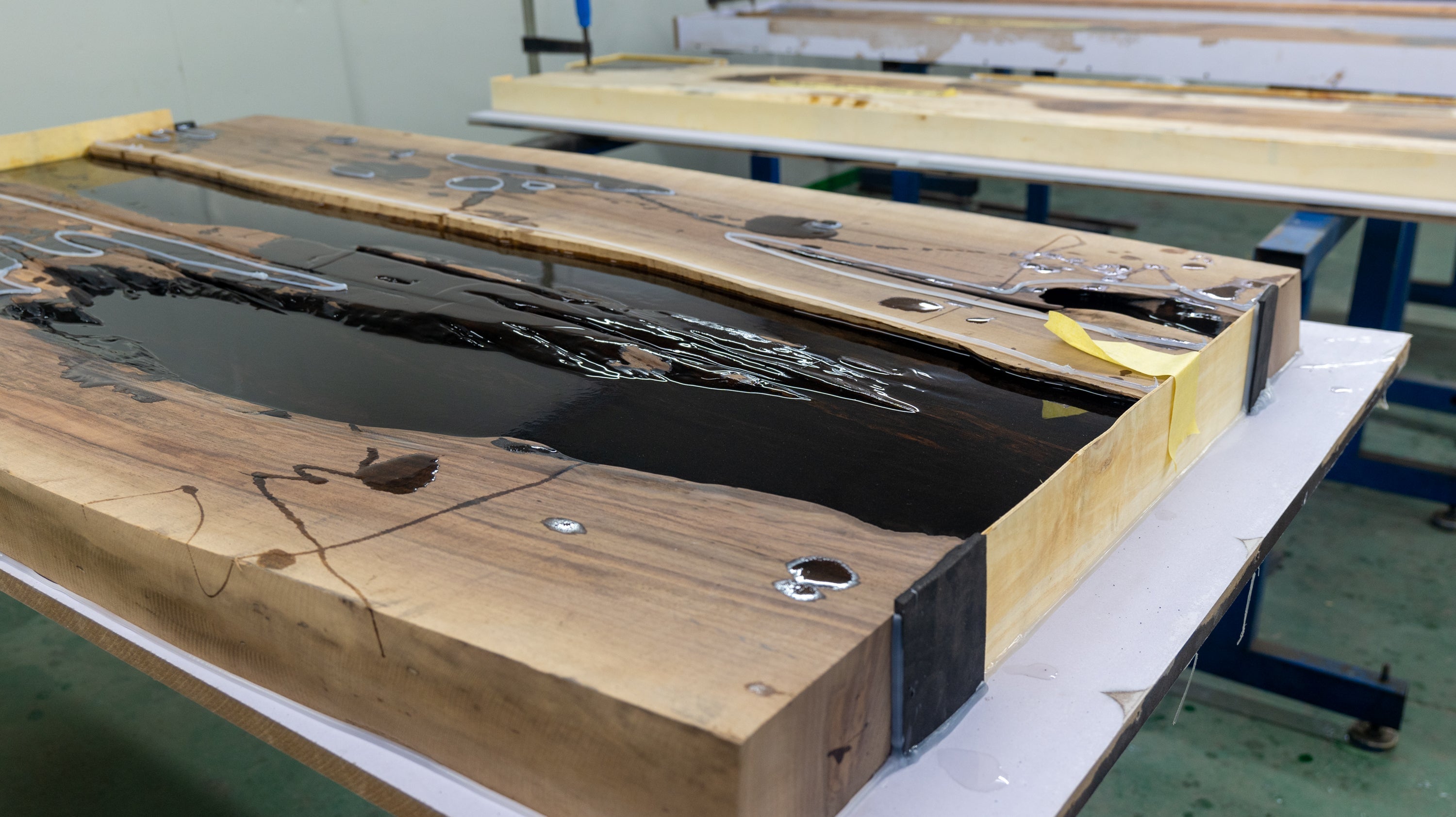 This image shows a wooden slab in a mold, with dark resin poured into its gaps, representing a key step in the epoxy resin table - making process as outlined in the "Complete Guide to Making Epoxy Resin Tables: From Preparation to Completion